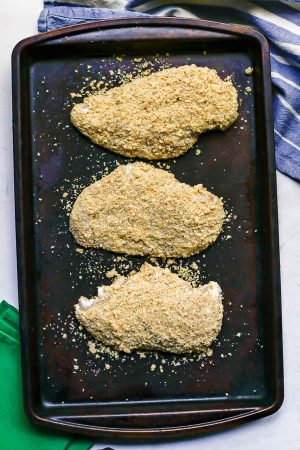 Breaded chicken breasts on a sheet pan before being baked in the oven