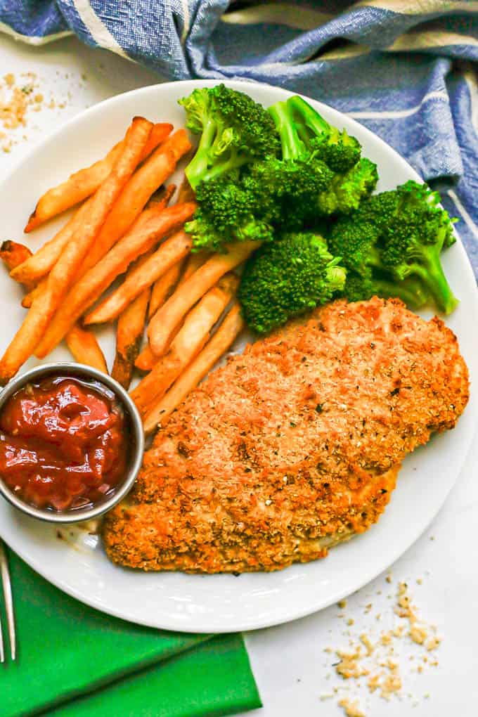 A white dinner plate with baked Ranch chicken, steamed broccoli and oven fries with a side of ketchup