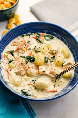 A spoon resting in a blue bowl of chicken gnocchi soup