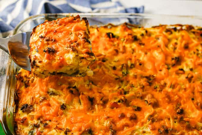 A spatula lifting up a piece of hash brown casserole from a baking dish