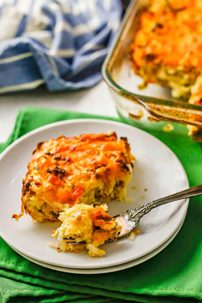 A forkful of hash brown casserole resting on a round white plate set on green napkins