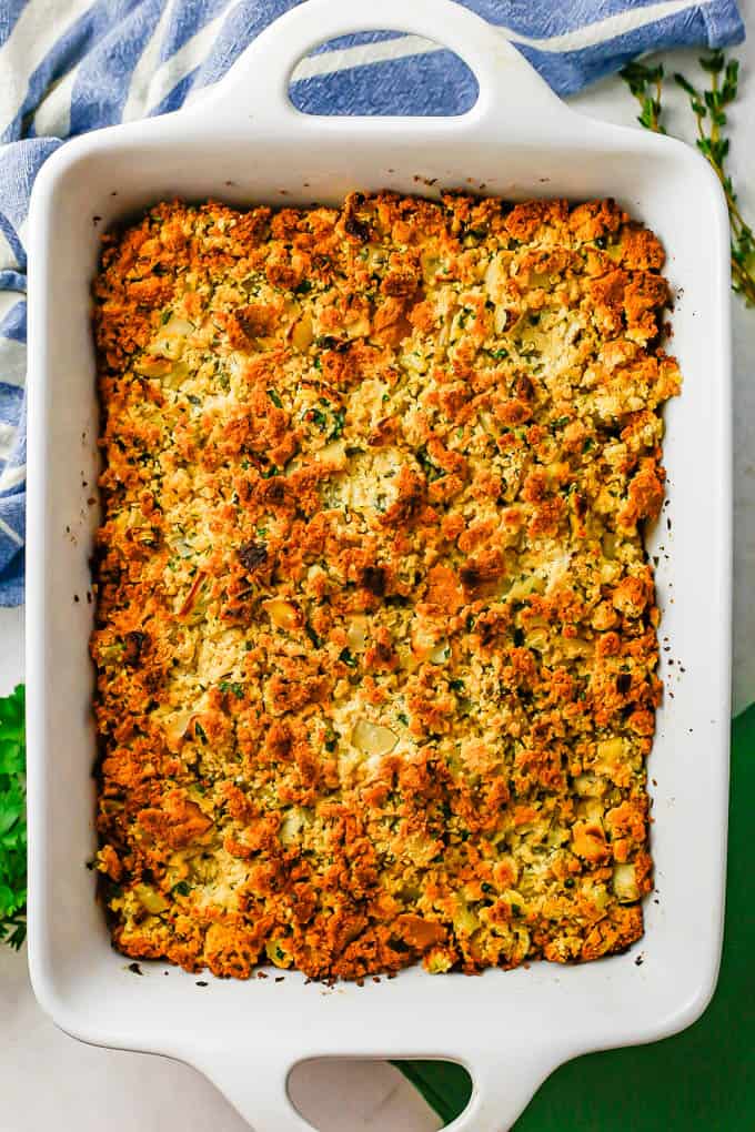 Southern cornbread dressing in a large white casserole dish after being baked with fresh herbs to the side