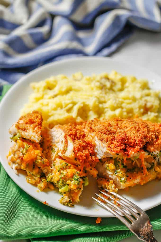 A fork resting on a white plate with a sliced broccoli cheese stuffed chicken breast served alongside mashed potatoes.