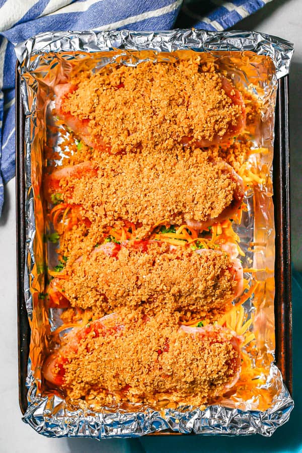 Breadcrumb coated stuffed chicken breasts on a foil lined baking sheet before being cooked