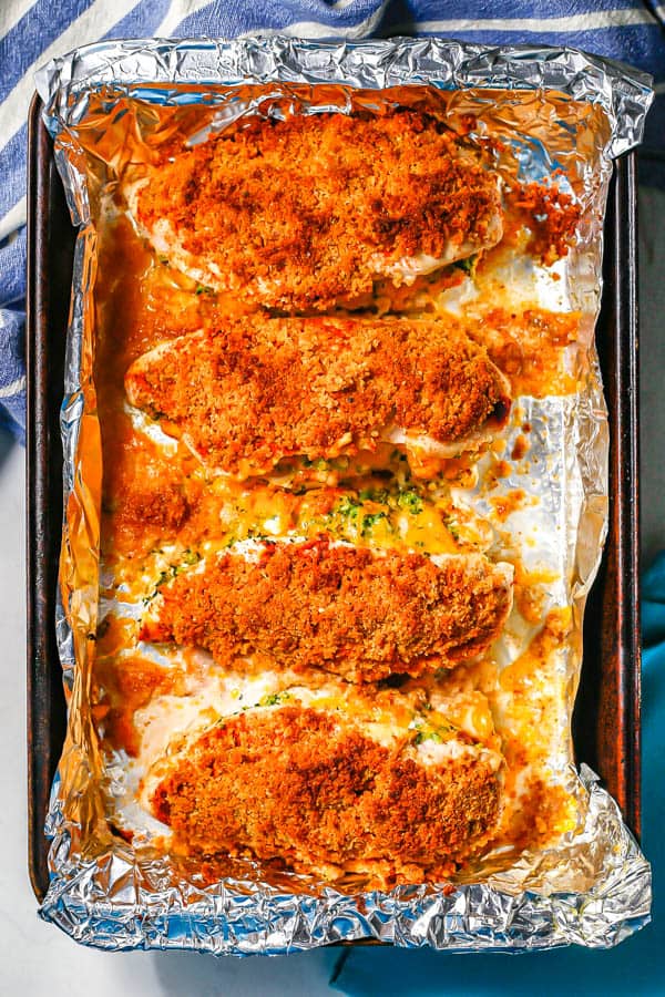 Crunchy golden brown broccoli cheese stuffed chicken breasts on a foil lined baking sheet after coming out of the oven.