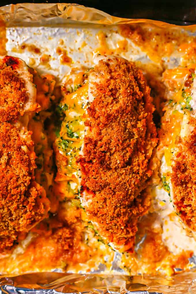 Close up of a broccoli cheddar stuffed chicken breast on a foil lined baking sheet after coming out of the oven.