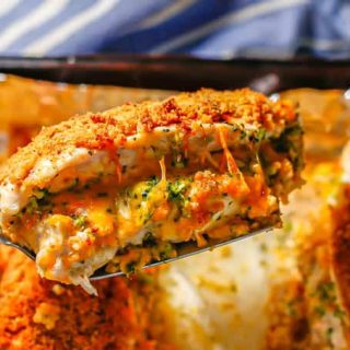A spatula lifting up a broccoli and cheese stuffed chicken breast with a breadcrumb coating from a baking sheet.
