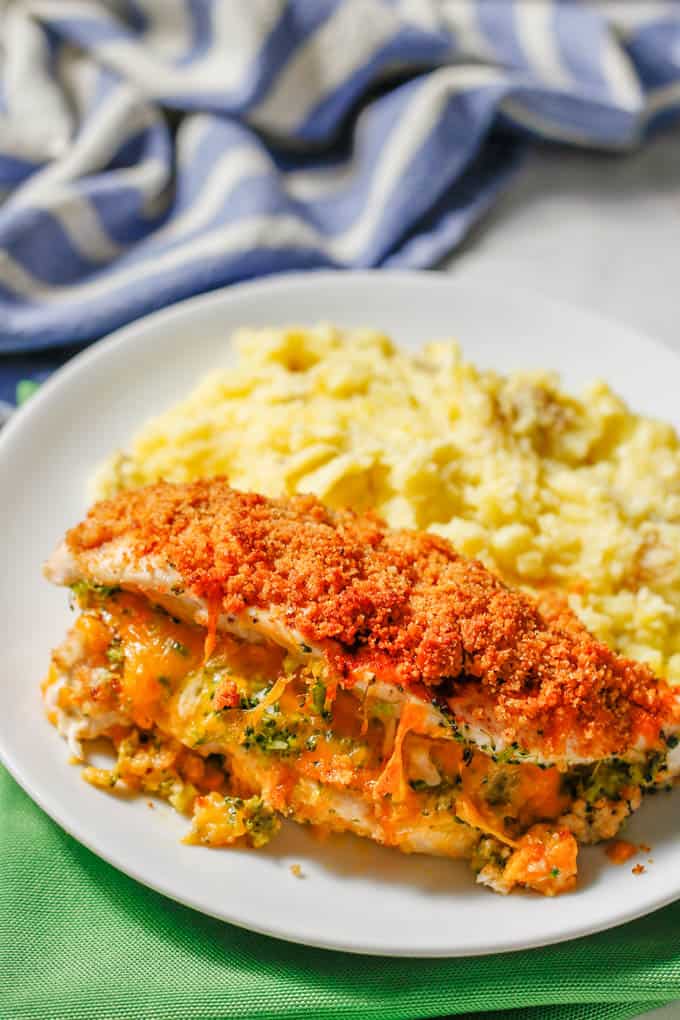 A broccoli cheese stuffed chicken breast served with mashed potatoes on a round white plate.