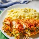 A fork resting on a white plate with a sliced broccoli cheese stuffed chicken breast served alongside mashed potatoes with a text overlay on the photo.