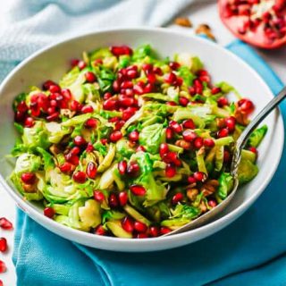 A white bowl with a mix of Brussels sprouts, pecan and pomegranate arils with a serving spoon resting in the bowl