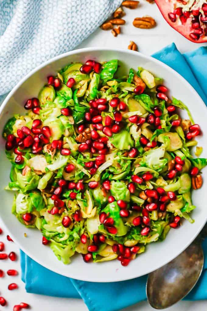 Overhead shot of shredded Brussels sprouts served in a low white bowl with toasted pecans and pomegranate arils