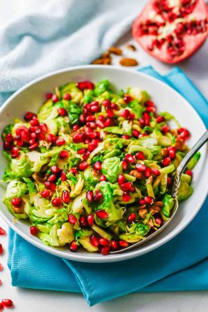 A festive mix of holiday Brussels sprouts with toasted pecans and pomegranate arils in a white serving bowl set on turquoise napkins