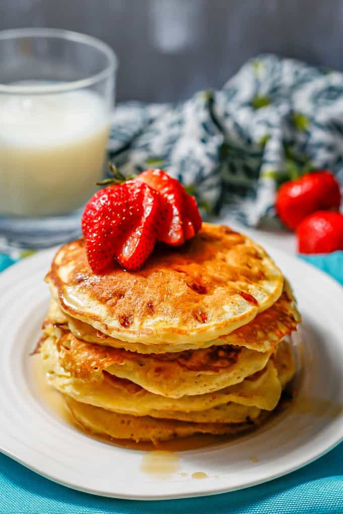Cottage cheese pancakes stacked on a white plate with maple syrup drizzled over and a sliced strawberry on top.
