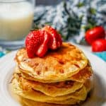 Cottage cheese pancakes stacked on a white plate with maple syrup drizzled over and a sliced strawberry on top and a text overlay on the photo.