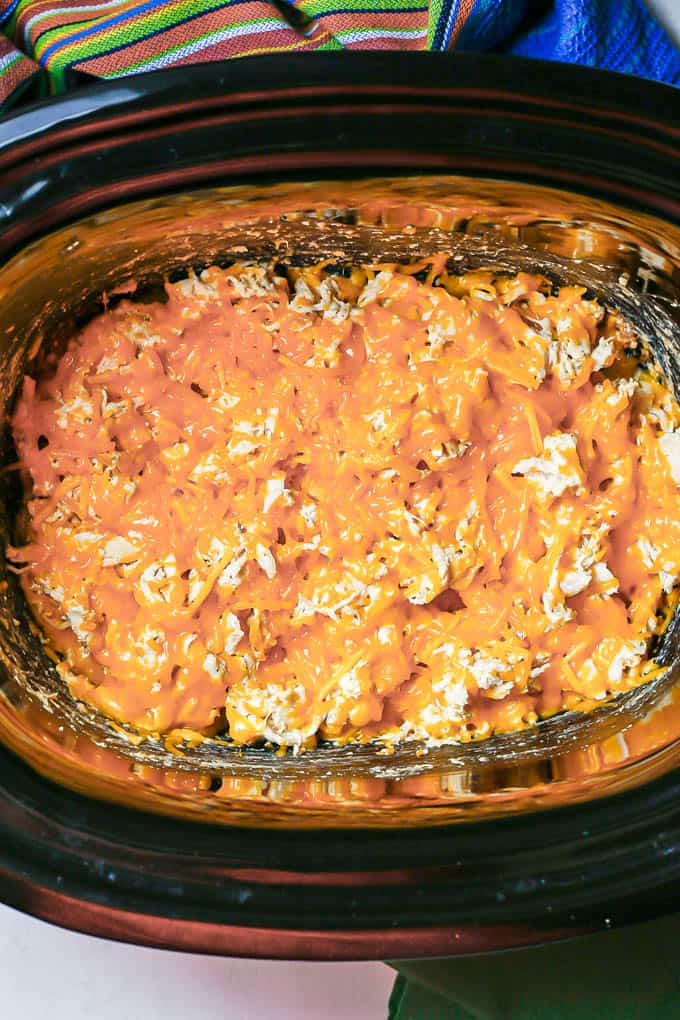 Melted cheddar cheese on top of a creamy shredded chicken mixture in a crock pot insert.