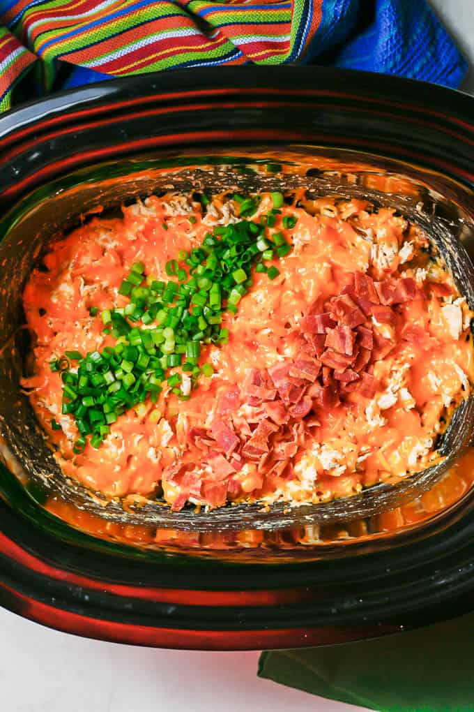Creamy cheese chicken in a slow cooker with chopped green onions and chopped cooked bacon on top.