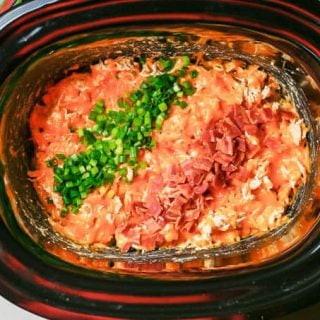 Creamy cheese chicken in a crock pot with chopped green onions and chopped cooked bacon on top.