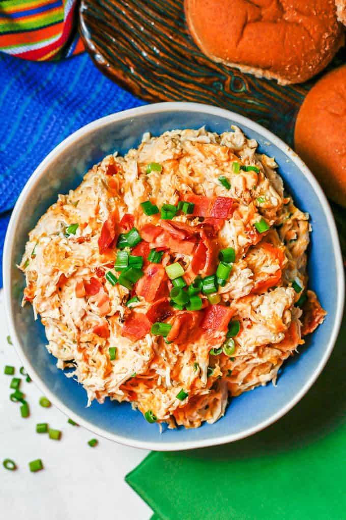 Crack chicken served in a blue bowl with a platter of soft buns nearby for serving.