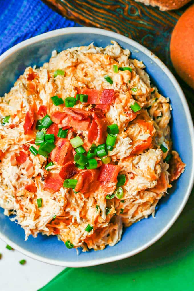 Close up of crock pot crack chicken served in a blue bowl with green onions and bacon on top.