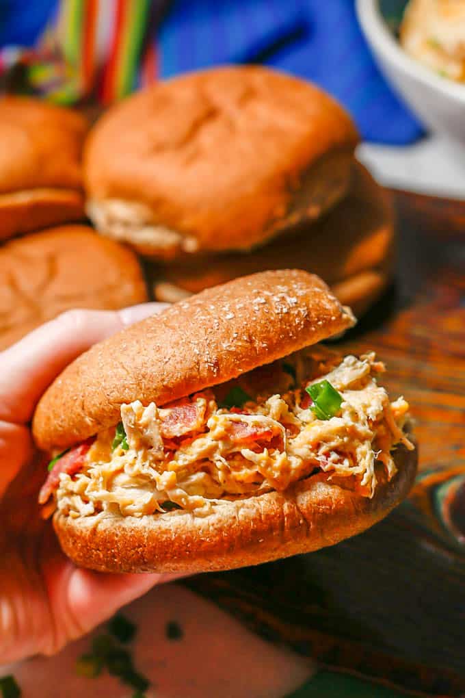 A hand holding up a wheat burger bun with crack chicken with bacon and green onions in it.
