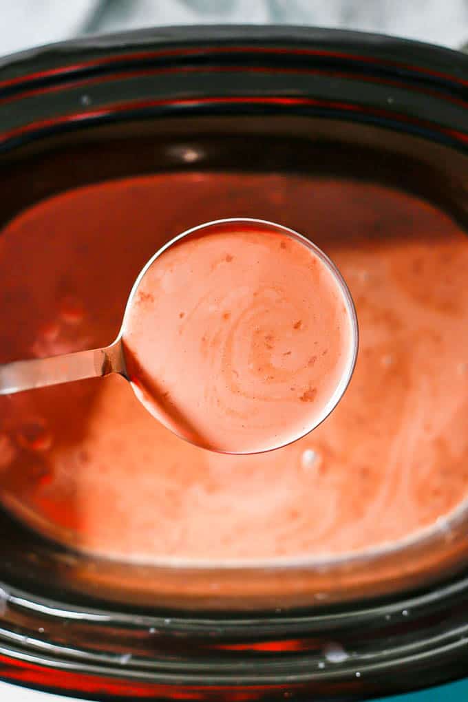 A ladle scooping hot chocolate from a crock pot insert