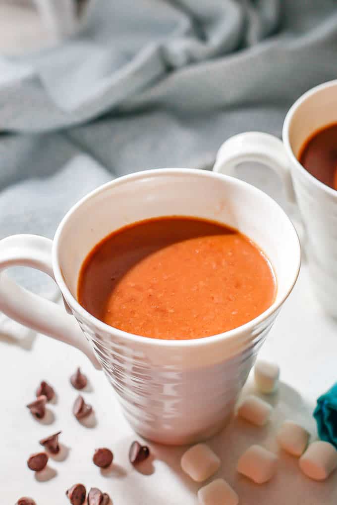 Hot cocoa served in white mugs with marshmallows and mini chocolate chips scattered at the base