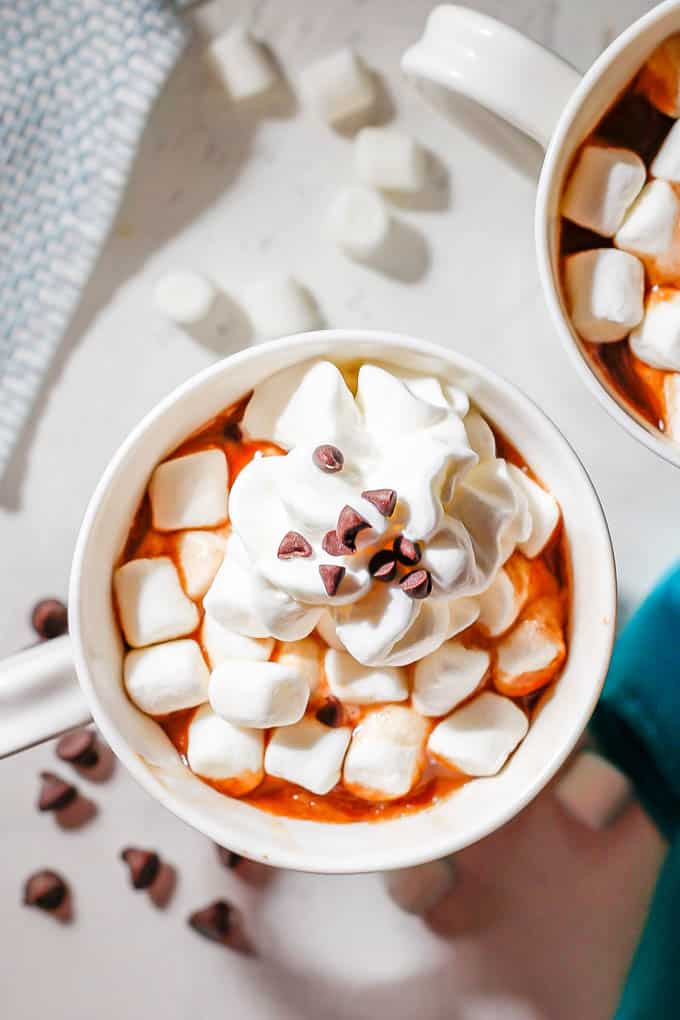 Overhead shot of mugs of hot chocolate topped with mini marshmallows, whipped cream and mini chocolate chips