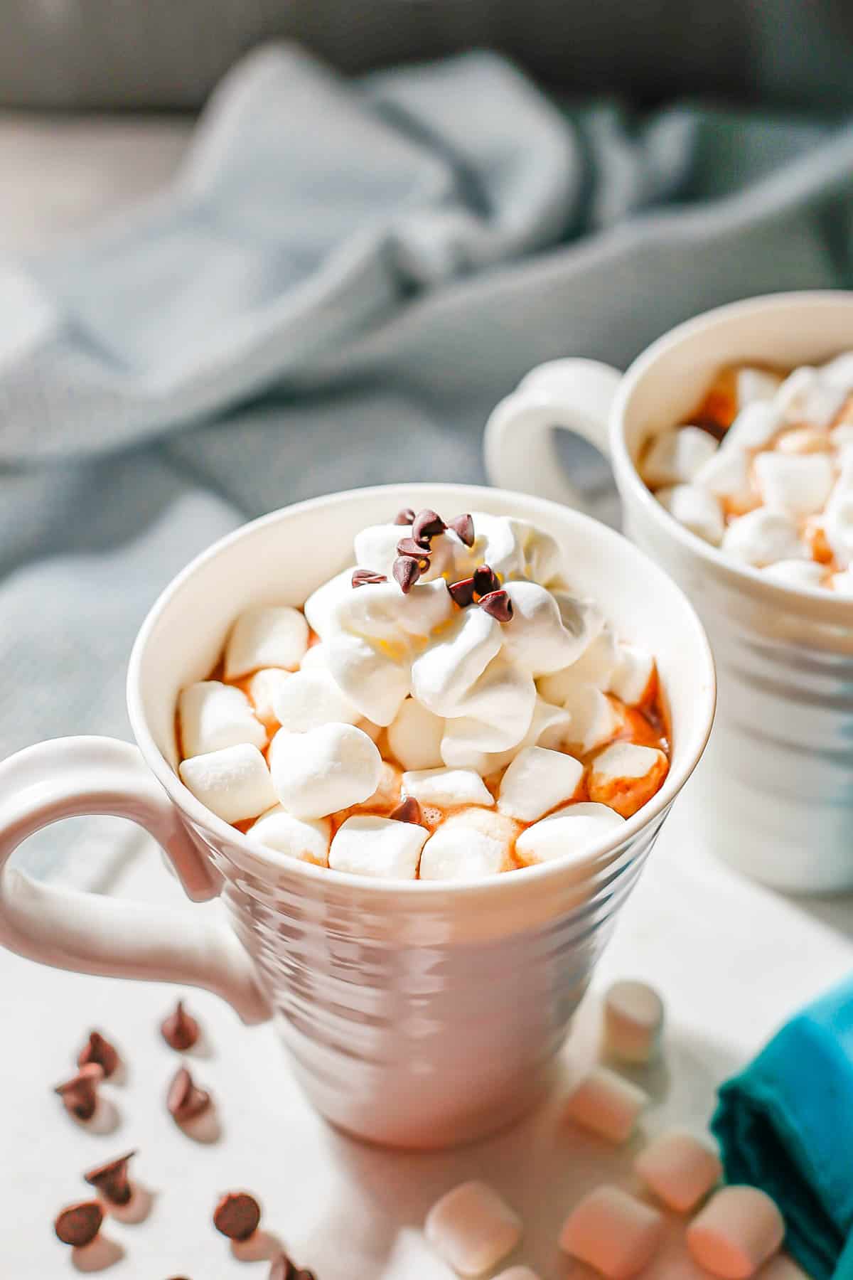 Hot chocolate served in white mugs and topped with mini marshmallows, whipped cream and mini chocolate chips