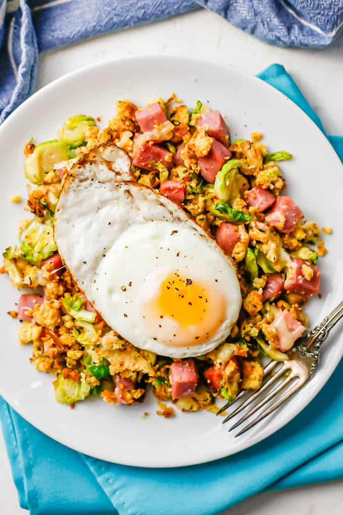 A fried egg on top of a breakfast hash with ham, cornbread dressing and shredded Brussels sprouts
