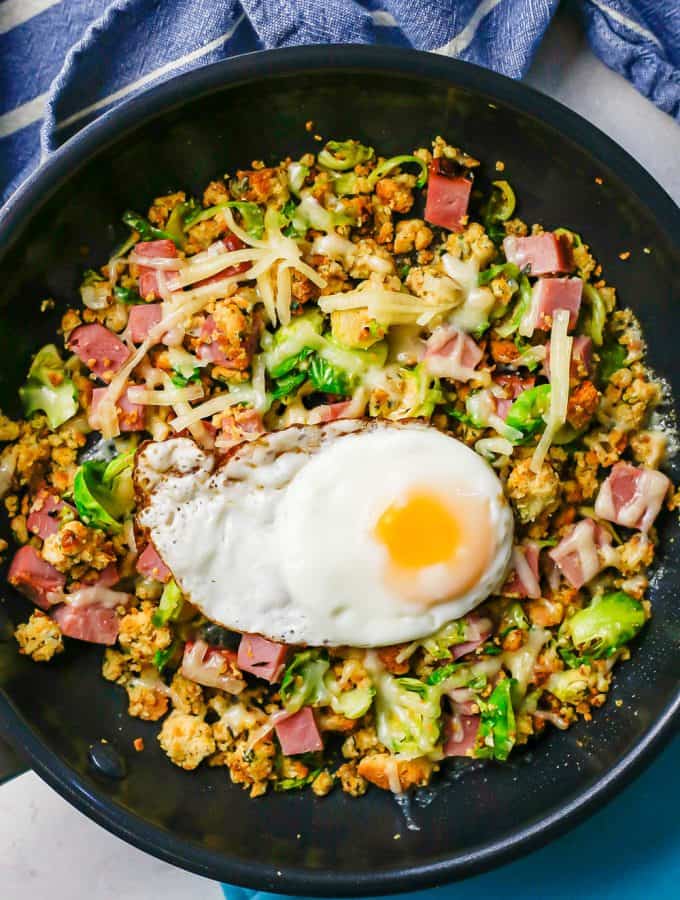 A large dark skillet with a ham breakfast hash topped with shredded cheese and a fried egg