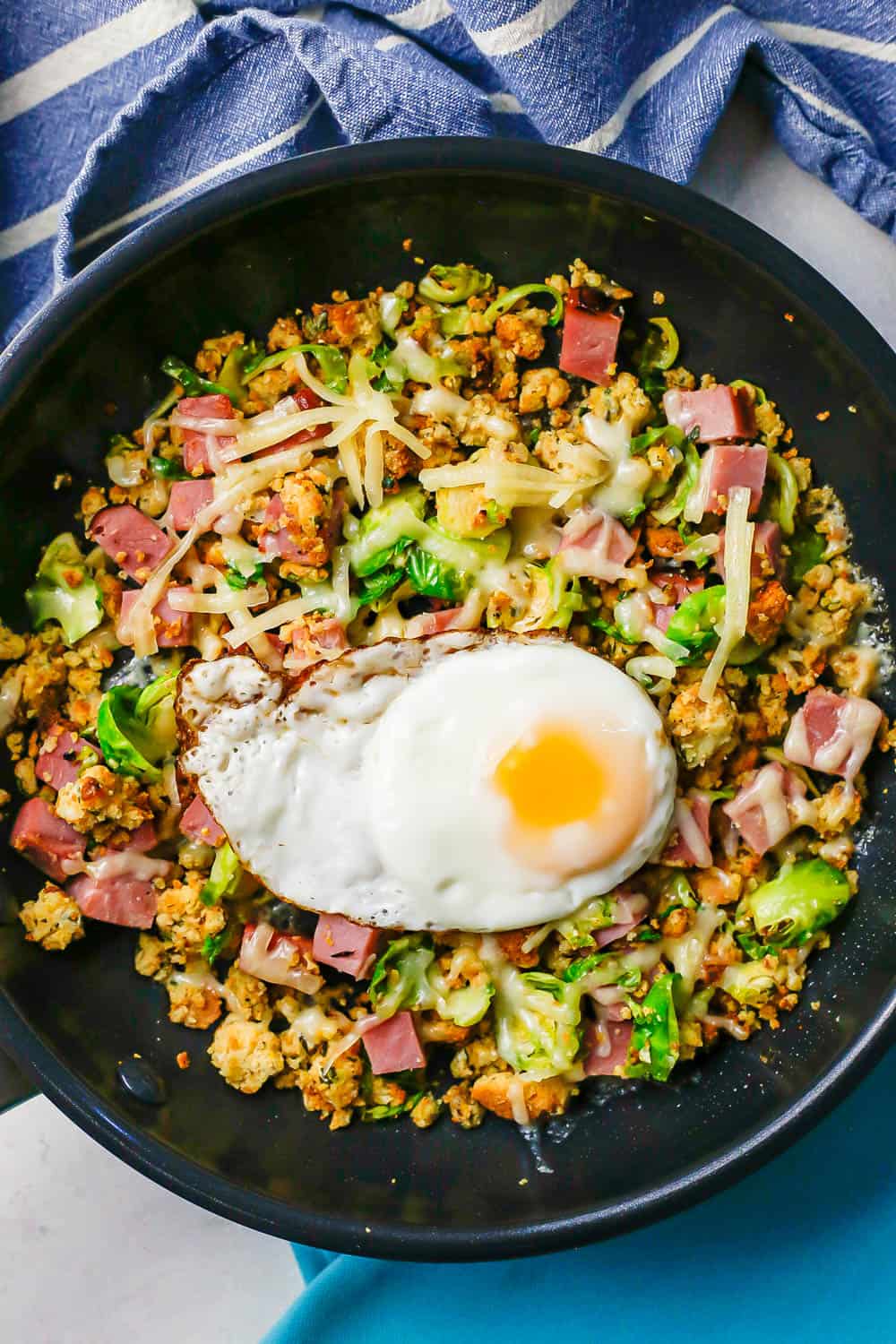 A large dark skillet with a ham breakfast hash topped with shredded cheese and a fried egg