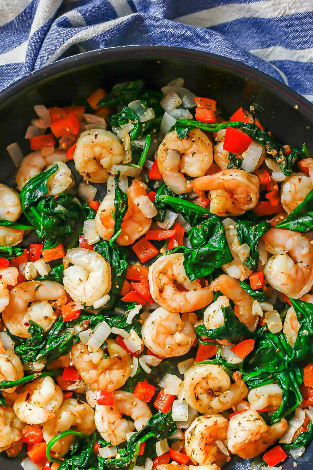 Close up of a skillet with shrimp, spinach, peppers and onions.