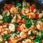 Close up of a skillet with shrimp, spinach, peppers and onions with a text overlay on top.