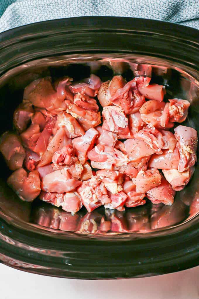 Cubed, seasoned chicken thighs in a slow cooker insert before being cooked.