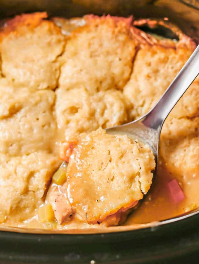 Close up of a spoonful of chicken and dumplings on a silver serving spoon in a slow cooker insert.