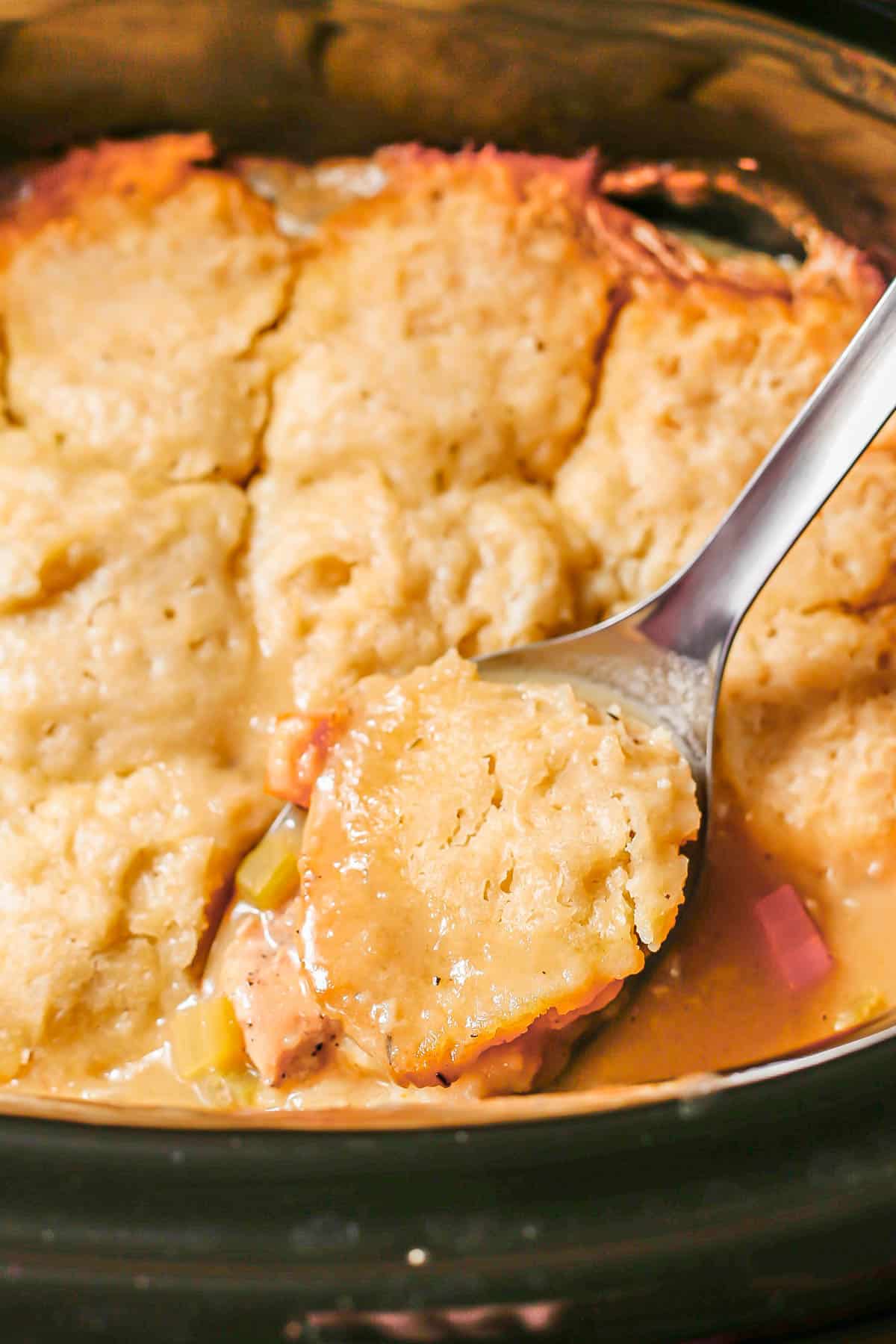 Close up of a spoonful of chicken and dumplings on a silver serving spoon in a slow cooker insert.