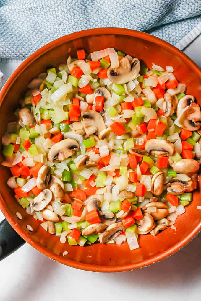 A large skillet with sautéed onion, celery, carrots and mushrooms.