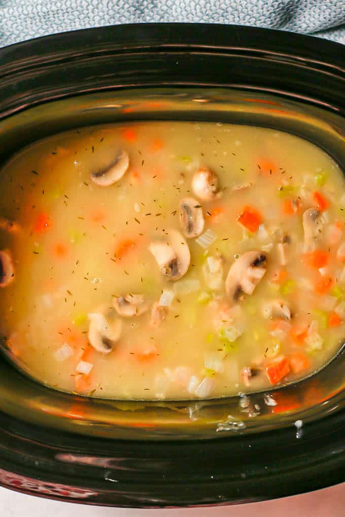 A chicken stew with mushrooms and veggies getting layered into a slow cooker before being cooked
