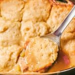 Close up of a spoonful of chicken and dumplings on a silver serving spoon in a slow cooker insert with a text overlay on the photo.