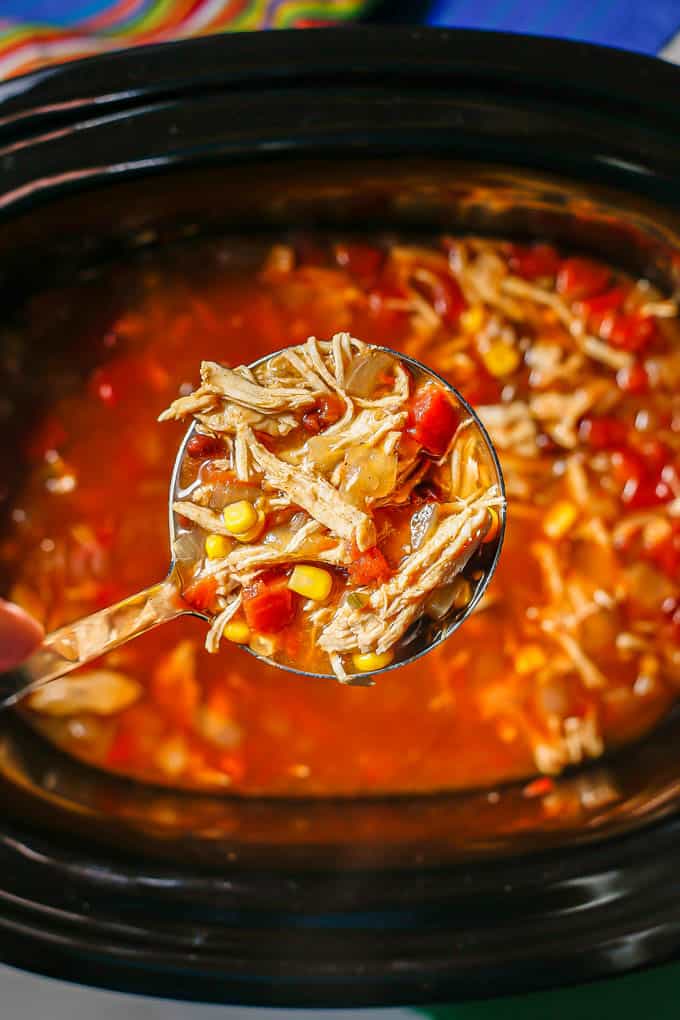 A silver ladle full of chicken tortilla soup being held over a crock pot
