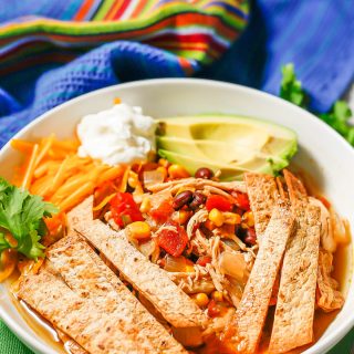 Chicken tortilla soup in a low white bowl with crispy tortilla strips, cheese, sour cream and avocado on top
