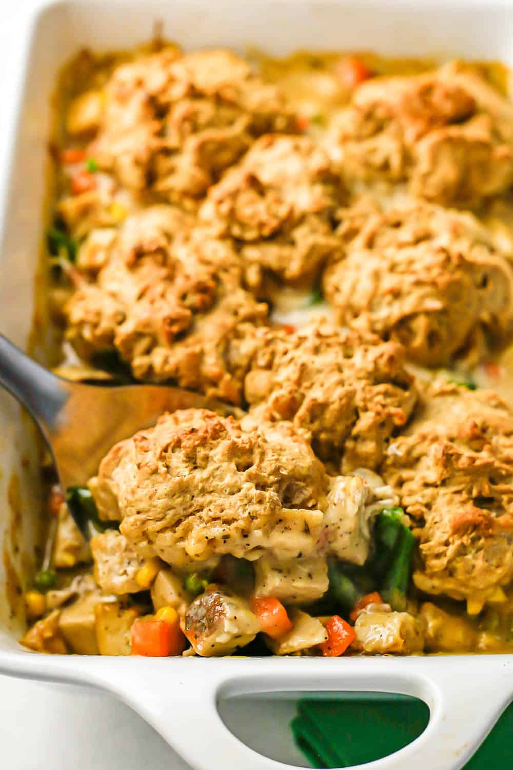 Close up of a scoop of turkey pot pie with a biscuit on top being taken from a white rectangular casserole dish