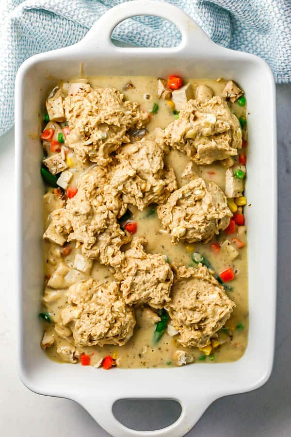 A rectangular white casserole dish with drop biscuits on a mixture of turkey and mixed vegetables in gravy