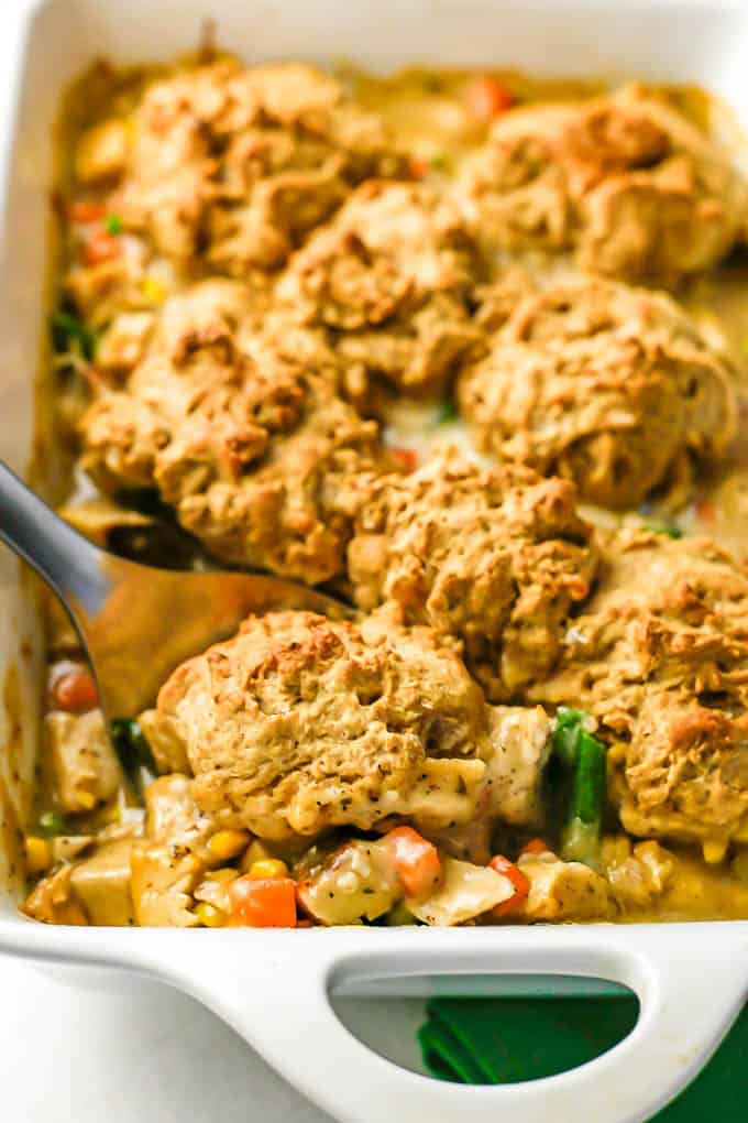 A spoon scooping out a drop biscuit and mixture of turkey and veggies in gravy from a casserole dish