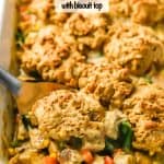 Close up of a scoop of turkey pot pie with a biscuit on top being taken from a white rectangular casserole dish with a text overlay on the image
