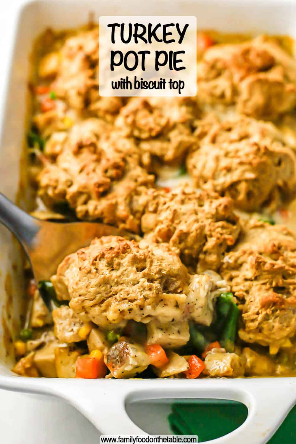Close up of a scoop of turkey pot pie with a biscuit on top being taken from a white rectangular casserole dish with a text overlay on the image