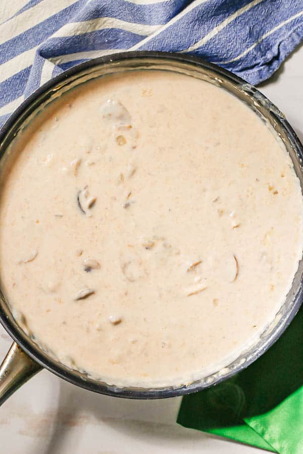 A cream sauce with onions and mushrooms being made in a large dark skillet
