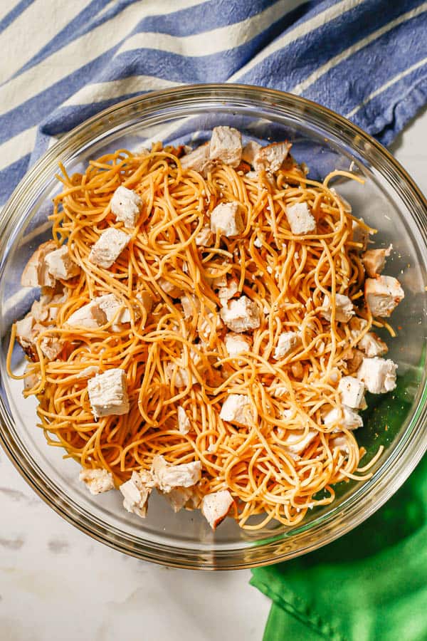 A mixture of cooked spaghetti and cooked chopped turkey in a large glass bowl