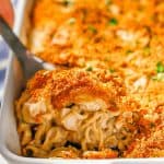 A silver spoon scooping up some creamy turkey tetrazzini with a breadcrumb topping from a white rectangular casserole dish with a text overlay on the photo