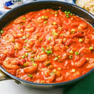 Easy shrimp creole in a large dark skillet with a bowl of rice nearby for serving.